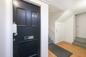 Une porte noire avec une fente pour le courrier, un escalier et un hall d’entrée recouvert d’un tapis.