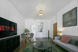 A modern living room with a flat-screen TV, a dining area, a sofa, and a large abstract painting. - Bon Accord Suite - Grampian Lettings (Aberdeen)