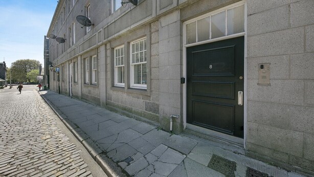 A building with a cobblestone street, large windows, and a black door with the number 8. - Bon Accord Suite - Grampian Lettings (Aberdeen)