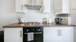 A kitchen with a gas stove, oven, white cabinets, a stainless steel range hood, and a coffee maker. - Bon Accord Suite - Grampian Lettings (Aberdeen)