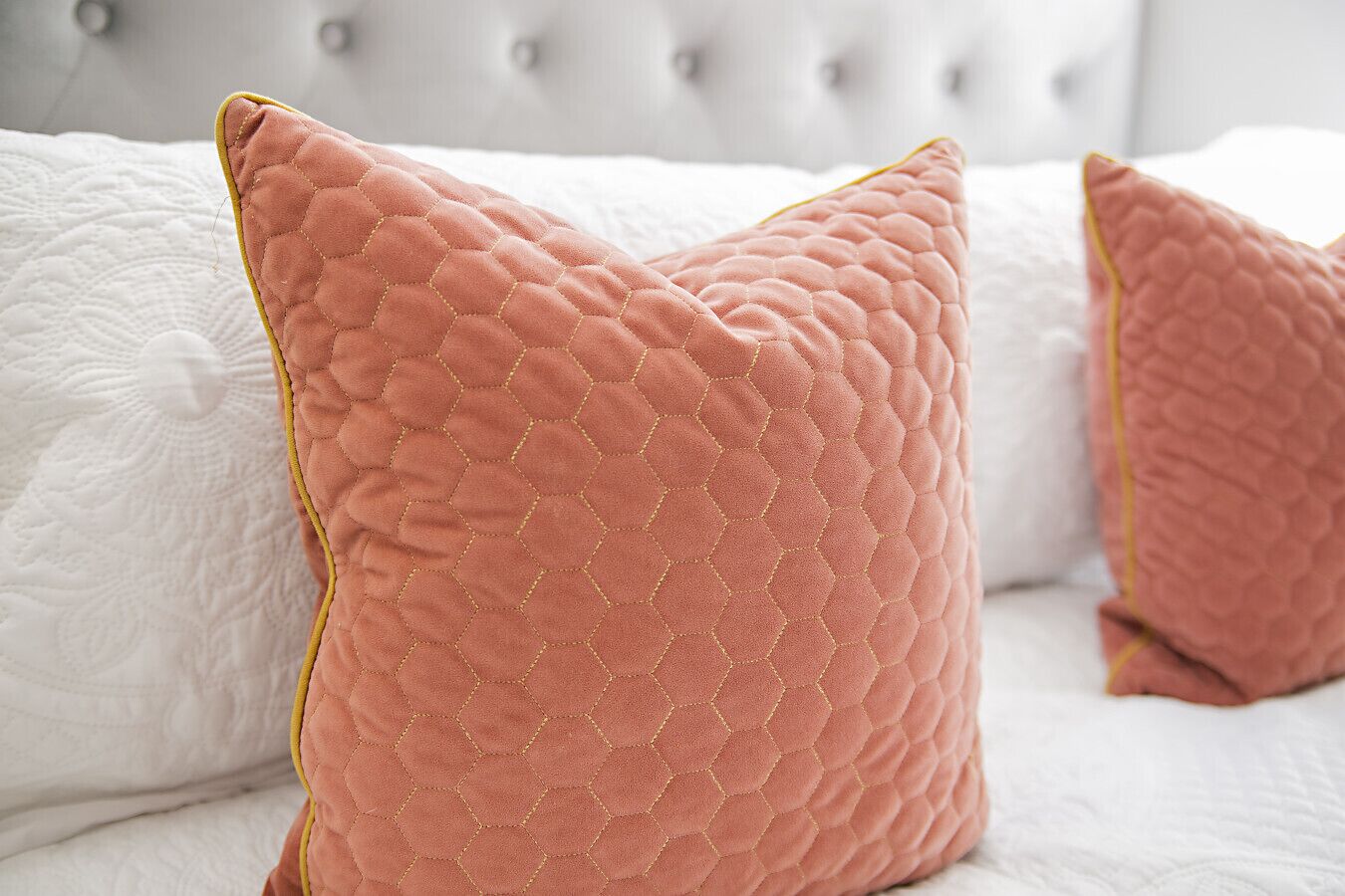 A bed with white bedding and two pink pillows with a honeycomb pattern.