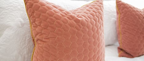 En säng med vita sängkläder och två rosa kuddar med ett bikakemönster.