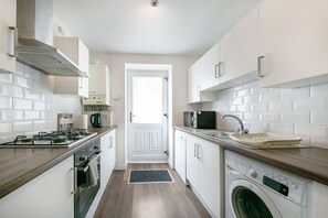 A modern kitchen with white cabinets, a stainless steel range, a microwave, a sink, and a washing machine. - Bon Accord Suite - Grampian Lettings (Aberdeen)