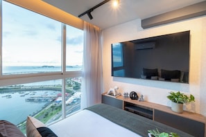 Ein modernes Hotelzimmer mit großem Fenster, einem Bett, einem Fernseher und einer kleinen Pflanze.