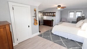 Et soveværelse med en seng, en guitar, en kommode og en loftsvifte.
