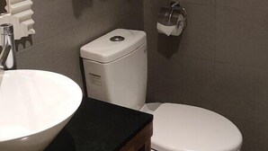 A bathroom with a white sink, toilet, and a towel rack with folded towels. - See S Revert Hotel (New Taipei City)
