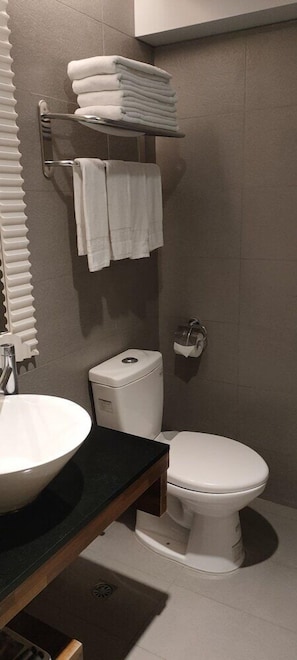 Un baño con lavamanos blanco, inodoro y toallero con toallas dobladas.