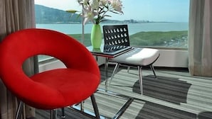 A hotel room with a large window, a red chair, a small table, a lamp, and a vase with flowers. - See S Revert Hotel (New Taipei City)