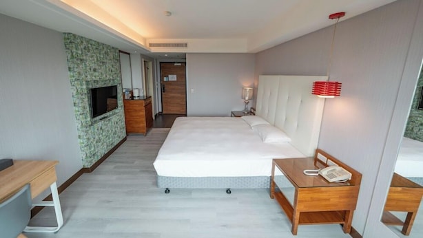 A modern hotel room with a large bed, a desk, a TV mounted on a textured wall, and a bedside table with a phone. - See S Revert Hotel (New Taipei City)