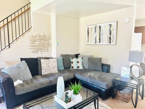 Ein Wohnzimmer mit Ecksofa, Couchtisch, Wandbild und einer Treppe.