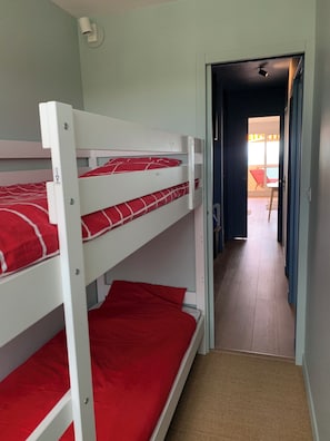 Een slaapkamer met stapelbed, vloerbedekking en een deur naar een balkon.