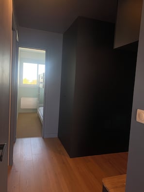 Een kamer met een houten vloer, een bed, een raam en een deur naar een andere kamer.