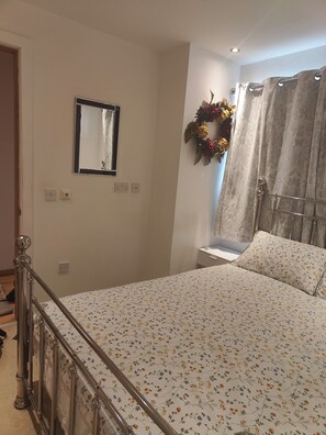 Ein Schlafzimmer mit einem Bett, einem Spiegel, einer Wandleuchte und einem Vorhang.