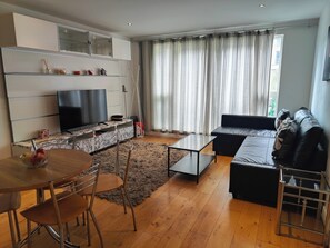 Ein modernes Wohnzimmer mit Flachbildfernseher, Sofa, Couchtisch und Essbereich mit Stühlen.