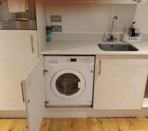 Eine kompakte Küche mit Einbauwaschmaschine, Spüle und kleiner Arbeitsplatte mit Seifenspender.