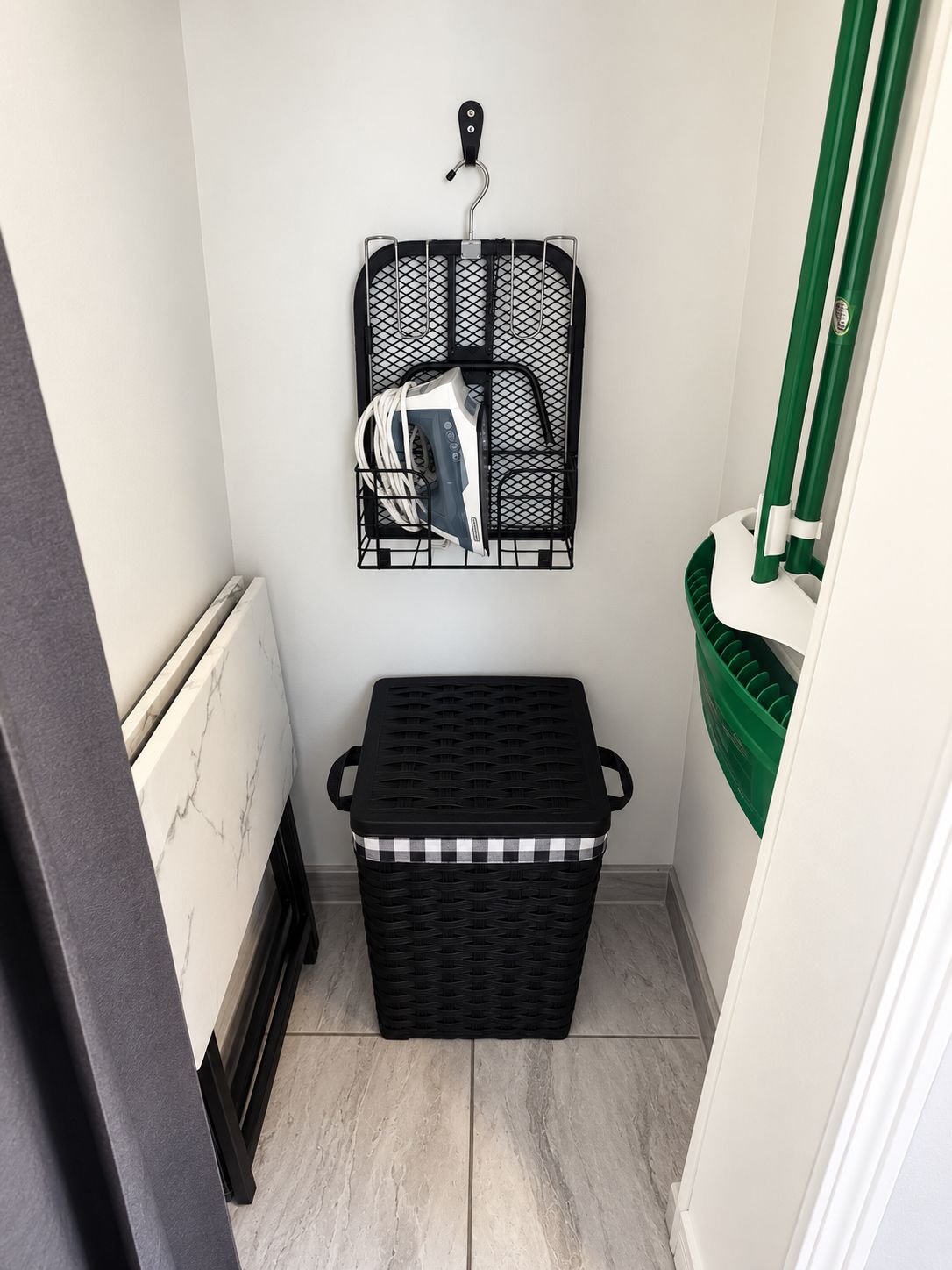 A small laundry room with a black basket, a hanging laundry rack, and a green storage bin.