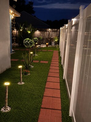 Ein Gartenweg mit künstlicher Beleuchtung, einem Holzzaun und einem Gebäude im Hintergrund.