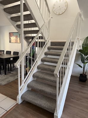 A staircase with carpeted steps and white railings, a clock on the wall, and a dining area with chairs and a table. - Old Town Art Stay • Luxe 3 Bedroom (Scottsdale)