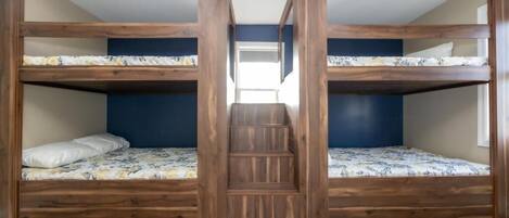 A room with two bunk beds, a wooden staircase, and a view of the hallway.