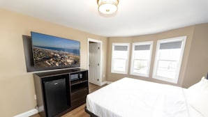 Un dormitorio con una cama, un televisor montado en la pared, un refrigerador negro pequeño y una puerta que da a otra habitación.