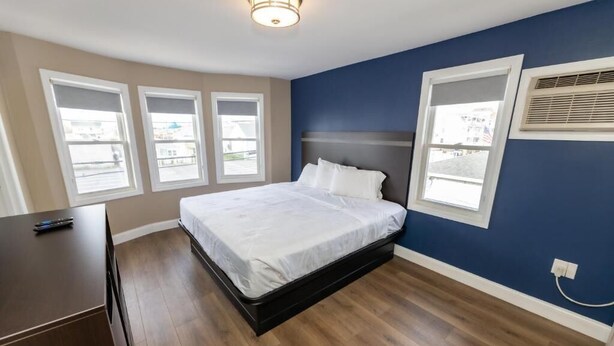 Un dormitorio con una cama, un aparador y tres ventanas.