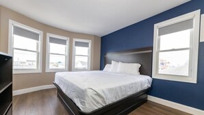 Un dormitorio con una cama, un televisor y tres ventanas.