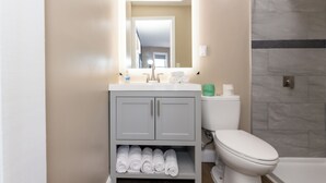 A bathroom with a toilet, sink, and mirror. There are towels on the counter and a shower area with a tiled wall. - Adjoining Room 2 - Spacious Two-Bedroom Suite Near Seaside Heights Beach, Sleeps 10 with Free WiFi  and  AC (Seaside Heights)