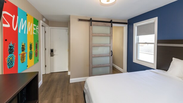 A bedroom with a bed, a sliding door, a wall with colorful artwork, and a ceiling light. - Adjoining Room 2 - Spacious Two-Bedroom Suite Near Seaside Heights Beach, Sleeps 10 with Free WiFi  and  AC (Seaside Heights)