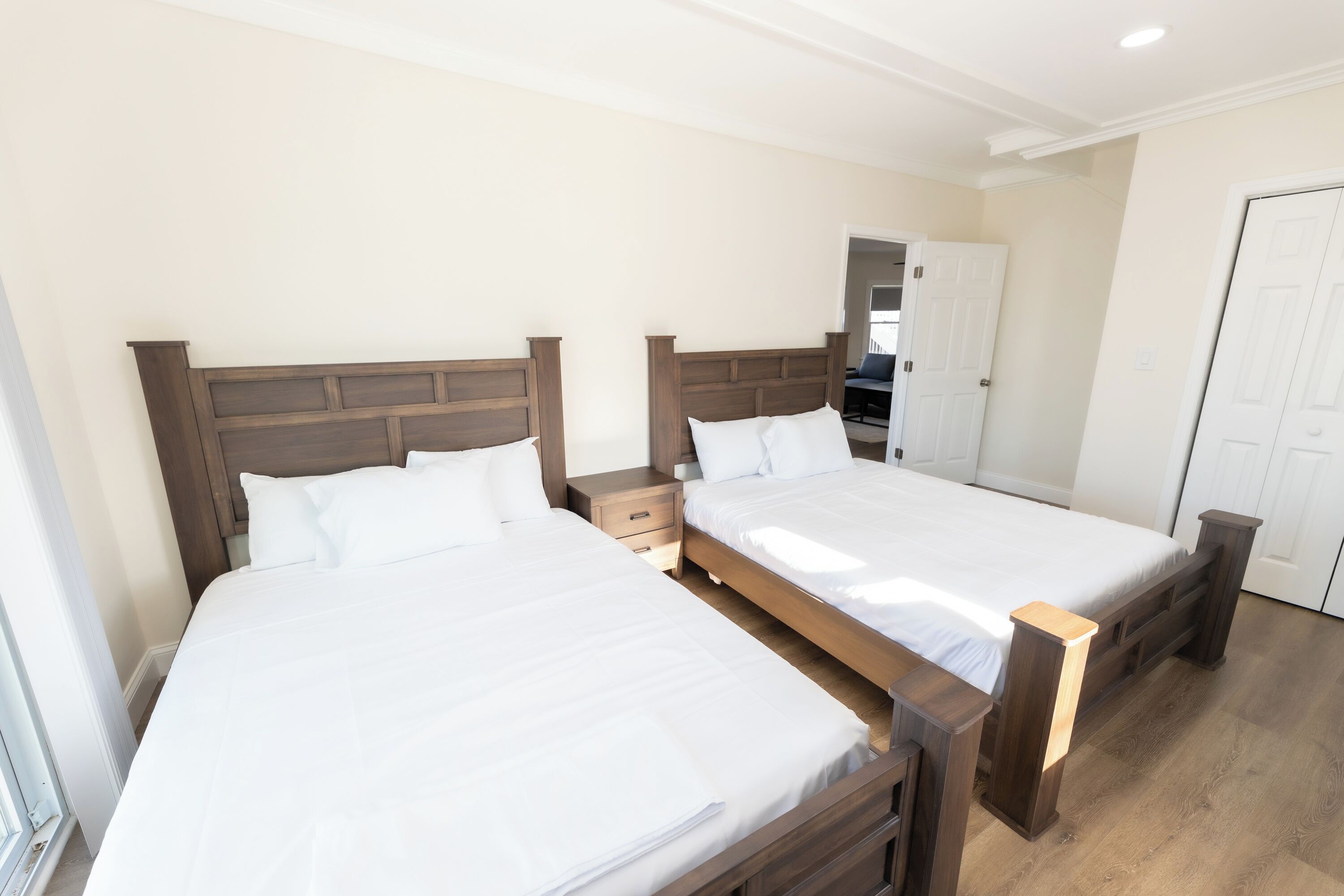 Ein Schlafzimmer mit zwei Betten, Holz-Kopfteilen, weißer Bettwäsche, einem Nachttisch und einer Tür.
