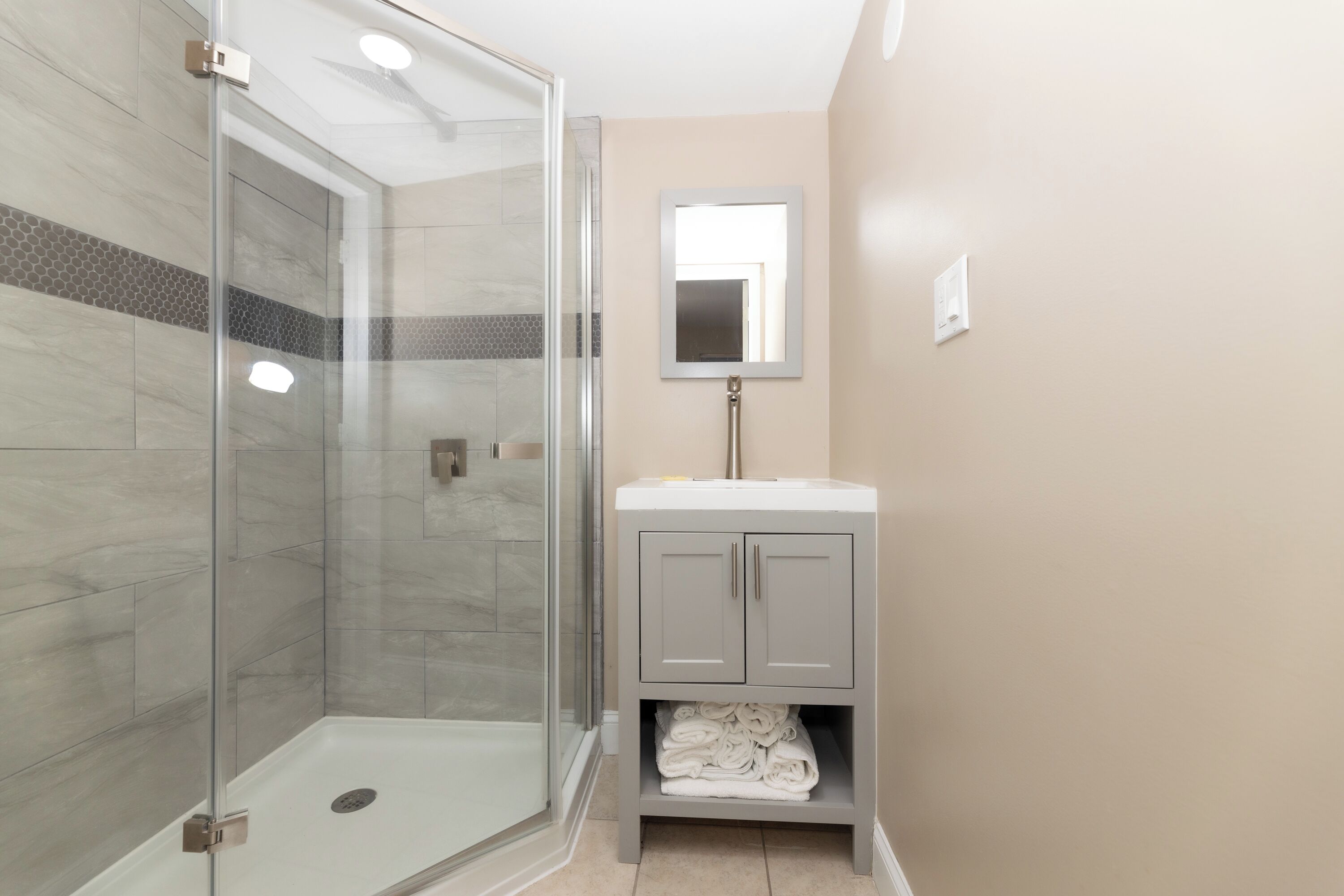 A bathroom with a glass shower enclosure, a sink with a mirror above it, and a cabinet below.