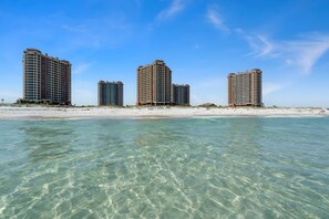 Ein Strandhotel mit mehreren Hochhäusern, klarem türkisblauem Wasser und einem Sandstrand.