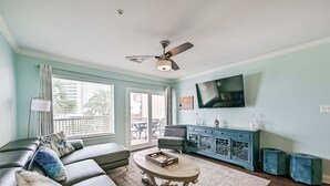 A living room with a sofa, coffee table, TV, and a ceiling fan. - Ocean View, Sea Ya Next Tide – 2 BR/2 BA - Sleeps 6 (Galveston)