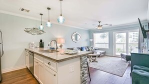 A kitchen with a central island, white cabinetry, and a dining area with a table and chairs. - Ocean View, Sea Ya Next Tide – 2 BR/2 BA - Sleeps 6 (Galveston)