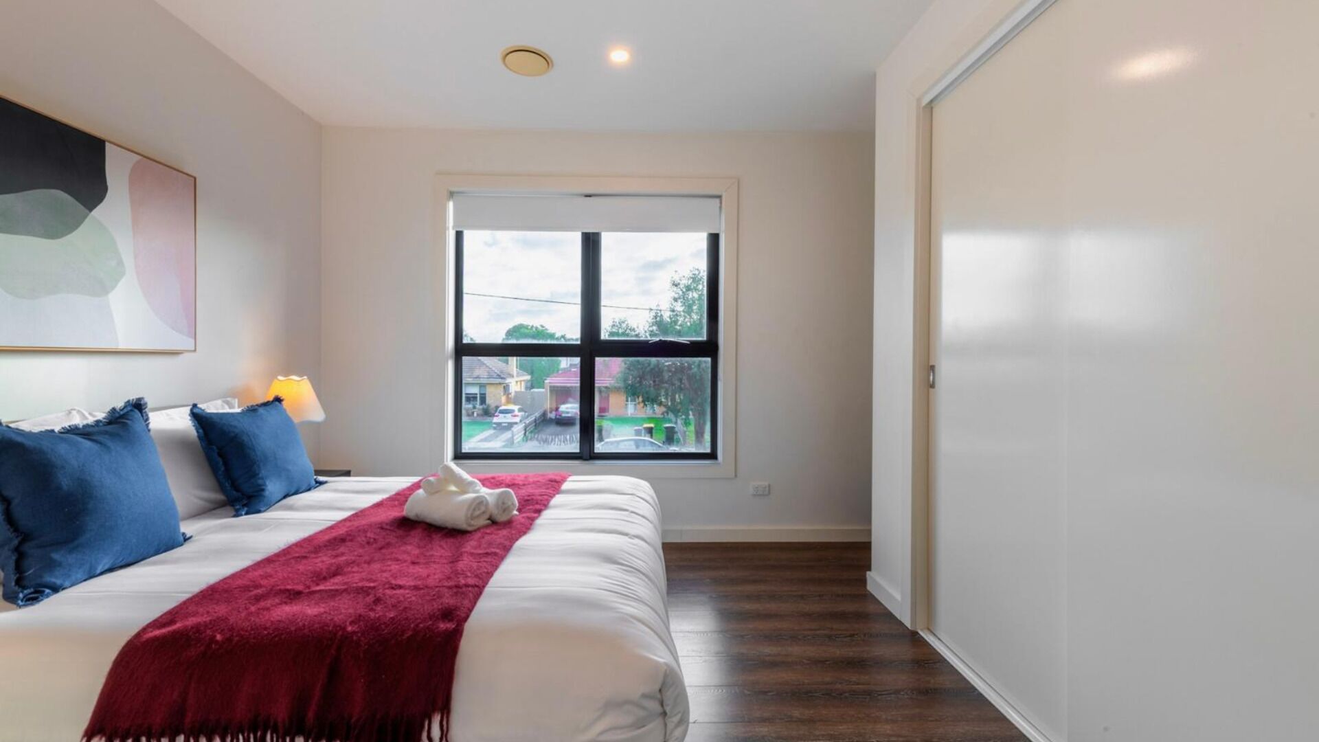 A bedroom with a bed, a window, a door, and a painting on the wall.