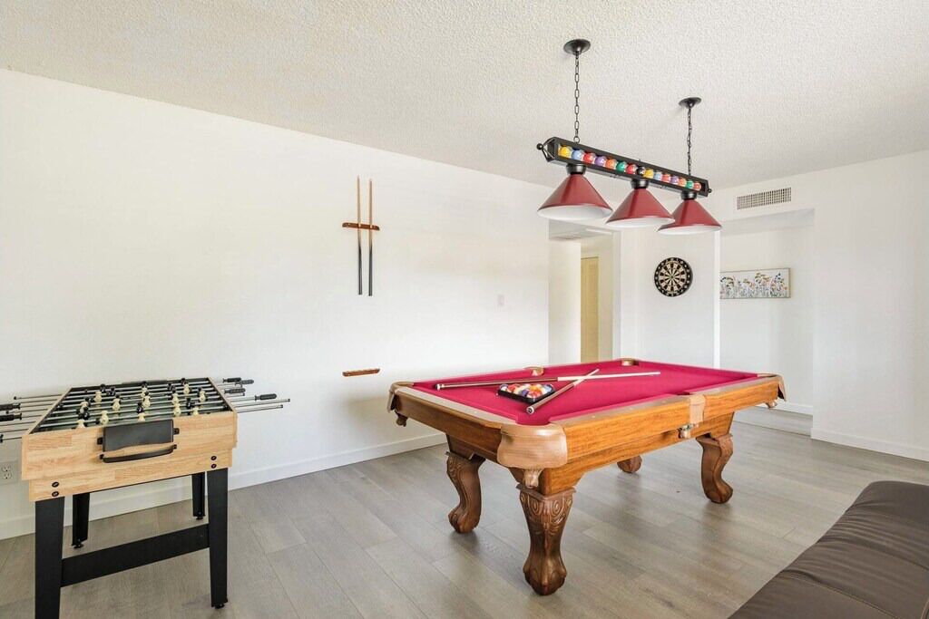 A room with a foosball table, a pool table, and two red pendant lights.