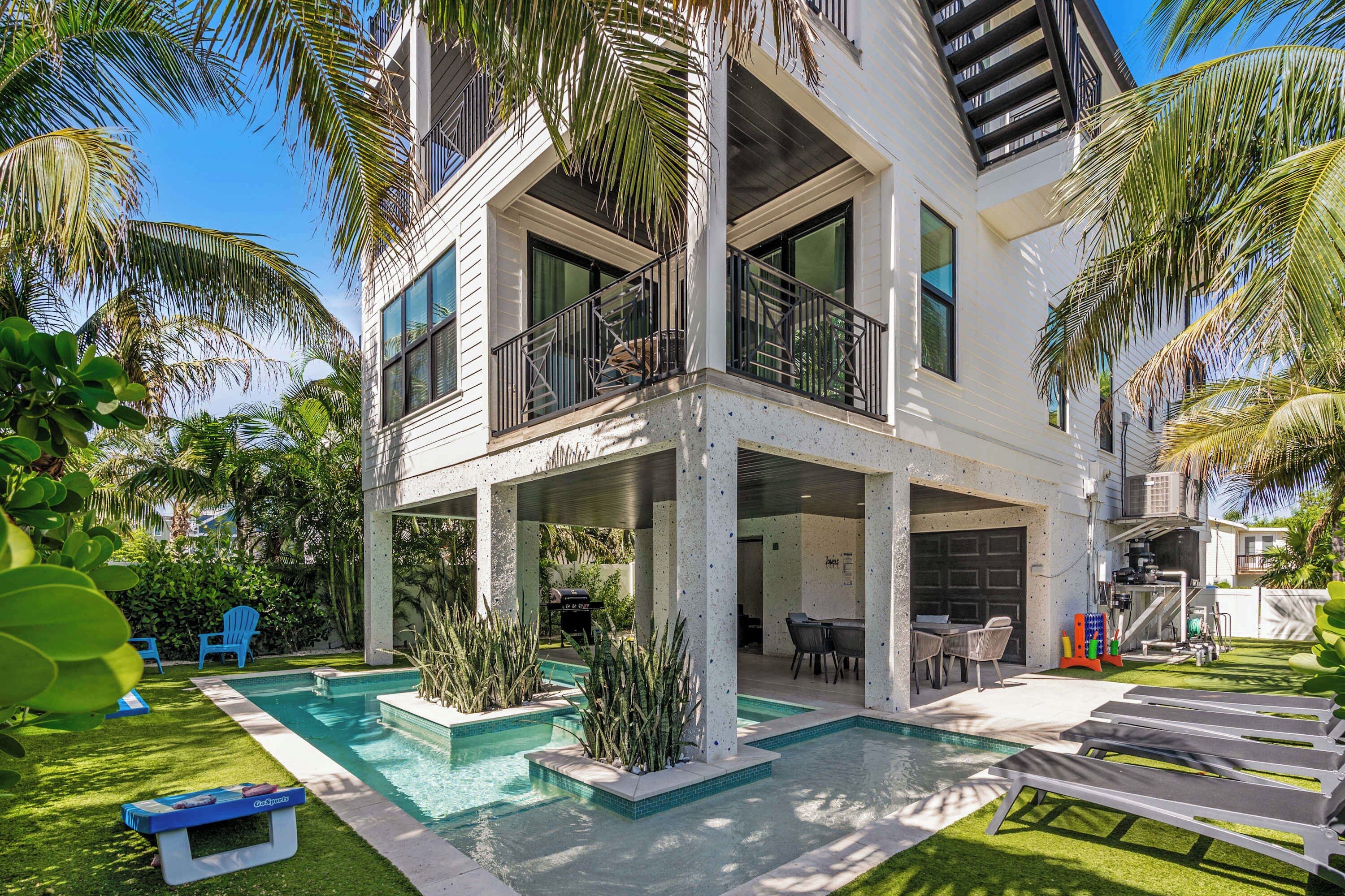 Una casa de dues plantes amb piscina, mobles d'exterior i plantes tropicals.