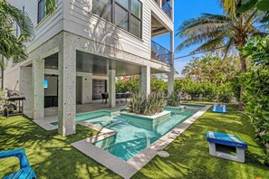 Ein modernes, zweistöckiges Haus mit überdachter Terrasse, Swimmingpool und üppiger Bepflanzung.