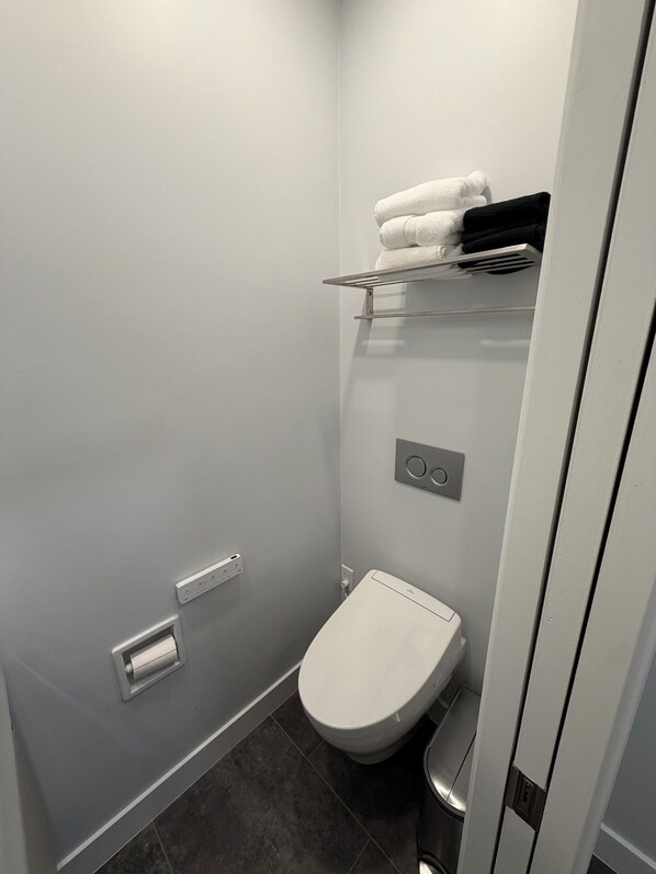 Un baño pequeño y moderno con inodoro, toallero y cubo de basura.