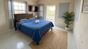 A bedroom with a bed, a TV, a window, a plant, and a balcony. - Pink Sands-At Bel Air (Belair)