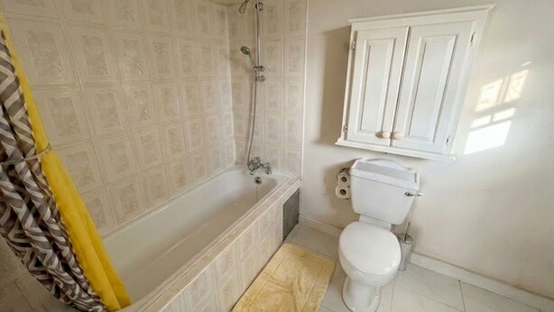A bathroom with a bathtub, toilet, and a cabinet. - Pink Sands-At Bel Air (Belair)