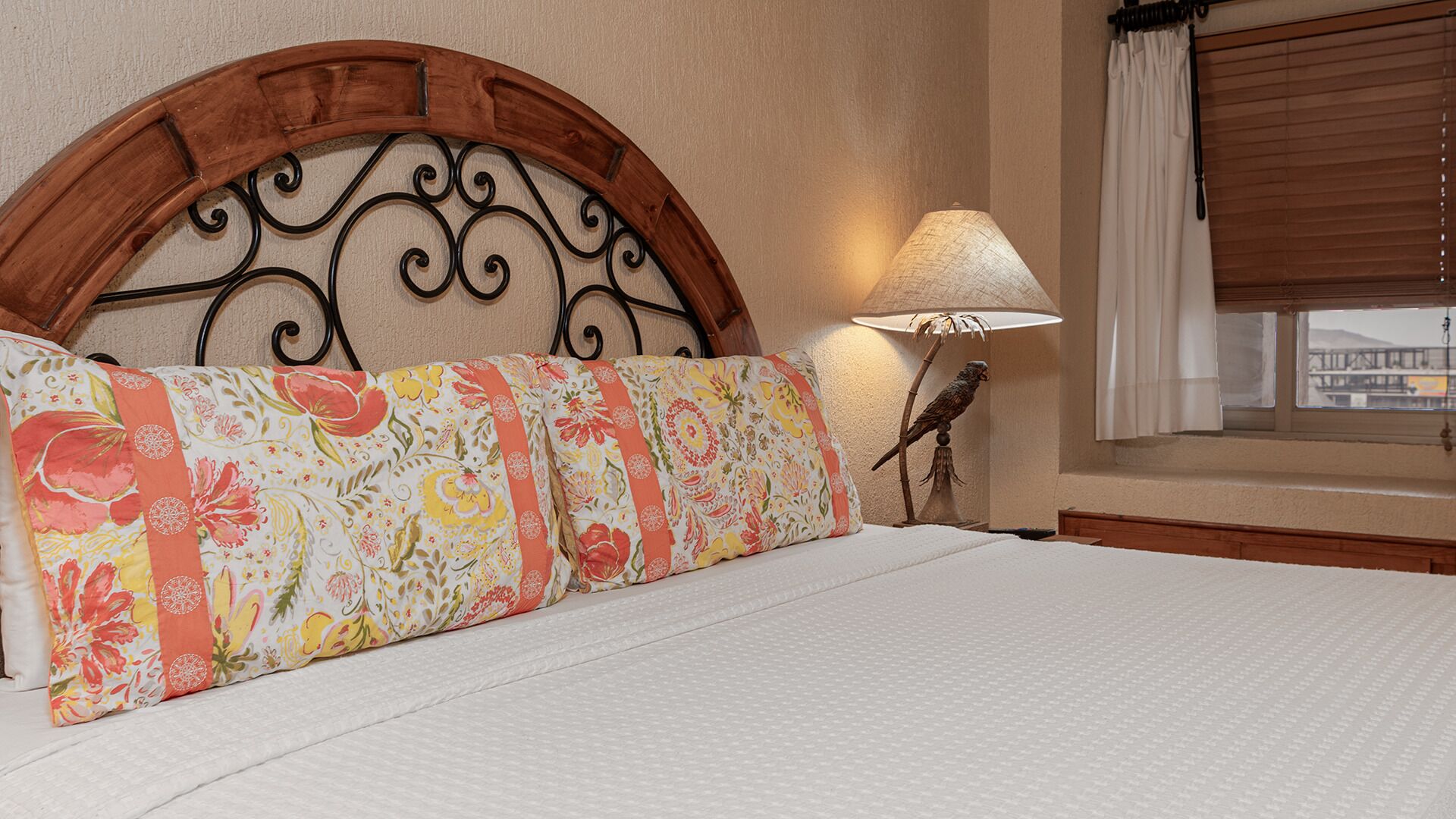 Une chambre d’hôtel avec un lit, une tête de lit décorative, une lampe et une fenêtre avec des rideaux.