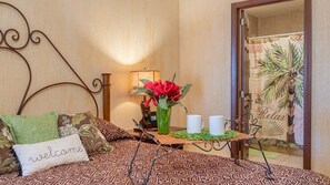 A bedroom with a patterned bedspread, a welcome pillow, a vase with red flowers, a tray with two white mugs, and a view of a palm tree through a curtain. - Sonoran Sun SW-414 Ocean Front Wraparound Terrace Condo (Puerto Peñasco)
