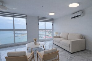 Un salon moderne avec une grande fenêtre, un canapé, une table basse et deux fauteuils.