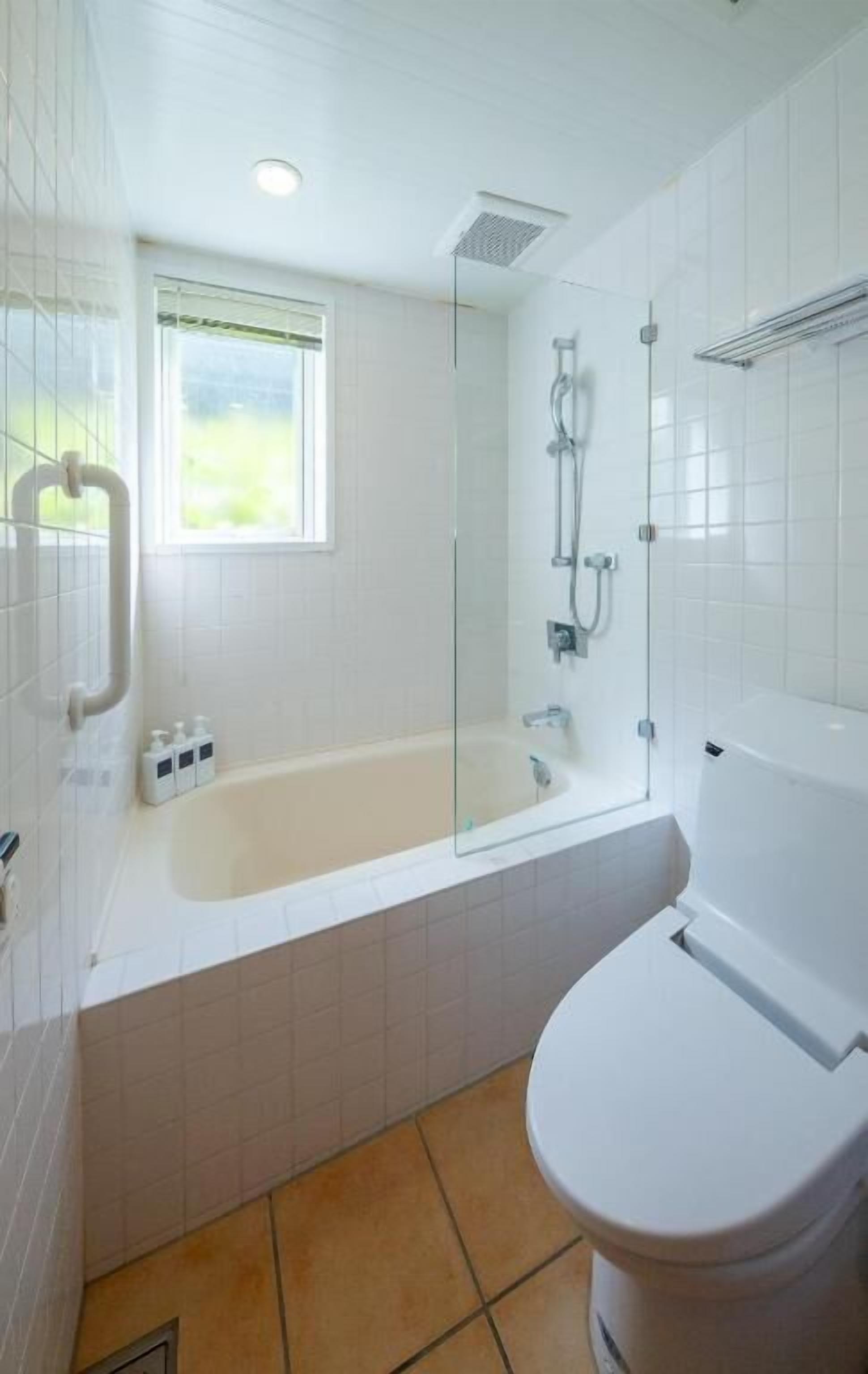 Casa de banho com chuveiro em cabine de vidro, banheira e sanita.