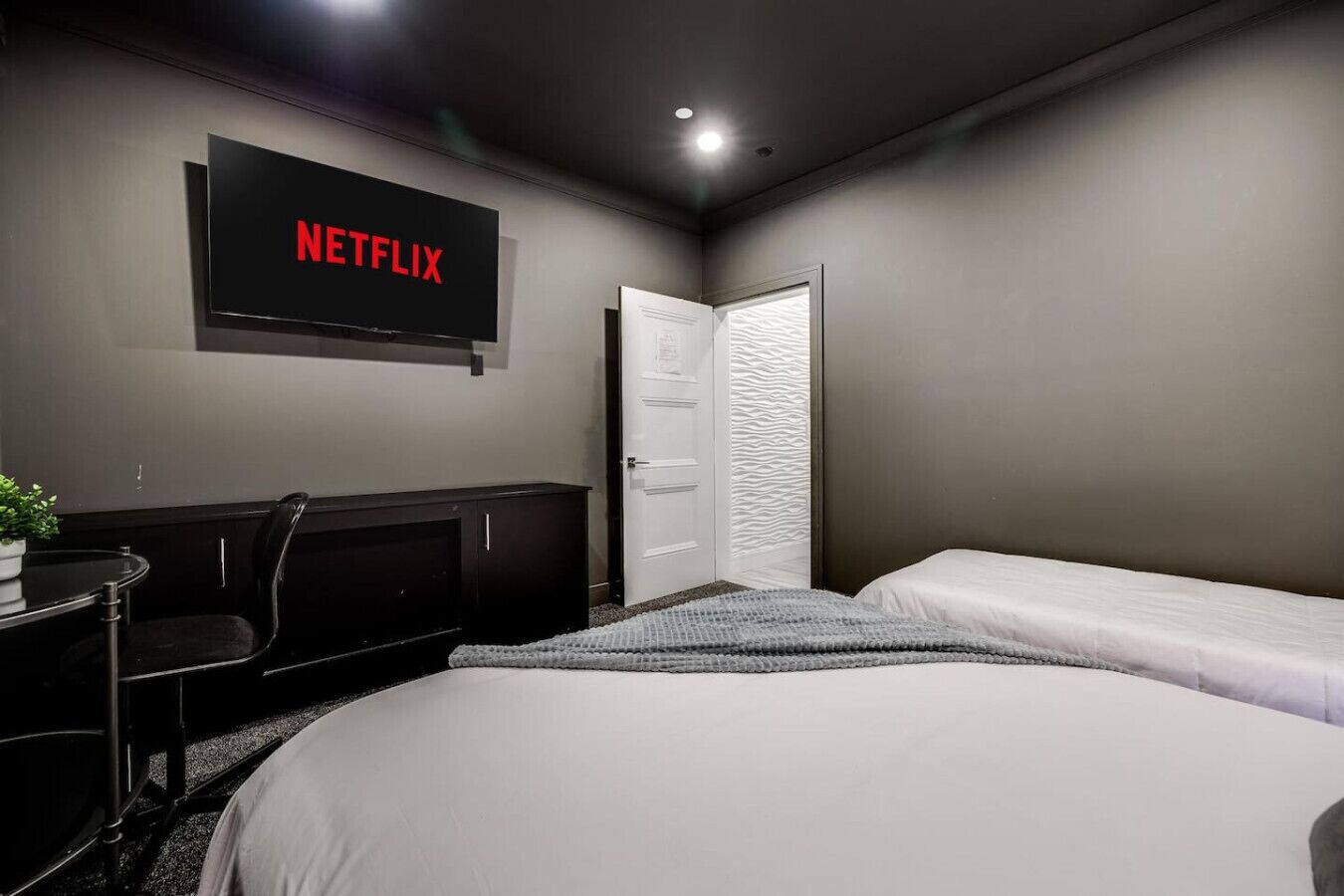 A bedroom with a bed, a desk, a chair, a TV mounted on the wall, and a door.