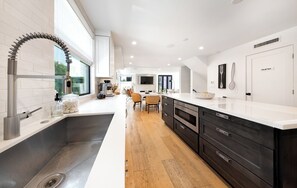 A modern kitchen with a large island, stainless steel appliances, and a view to the outdoors. - Luxury Marina del Rey Beach House with Rooftop Fire Pit + Walk to Beach (Los Angeles)