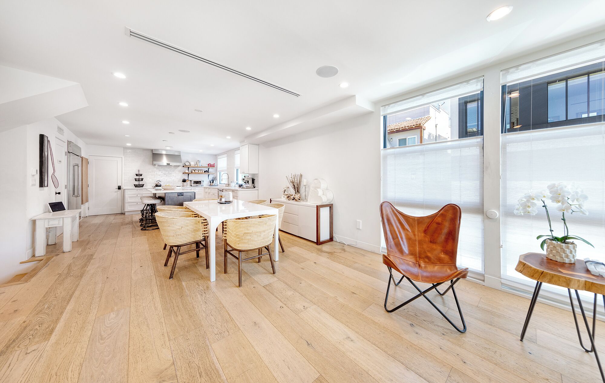 A spacious kitchen with white cabinetry, a dining area with a white table and wicker chairs, and large windows offering a view.