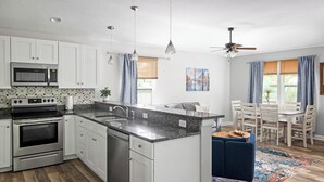 Eine moderne Küche mit weißen Schränken, einer Arbeitsplatte aus Granit, einem eingebauten Ofen und einem Essbereich mit blauem Stuhl und Holztisch.