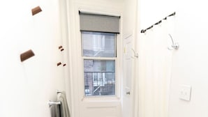 A bathroom with a window, a towel rack, a shower curtain rod, and a small rug.