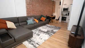 A modern living room with a sectional sofa, a dining area, and a kitchen in the background.